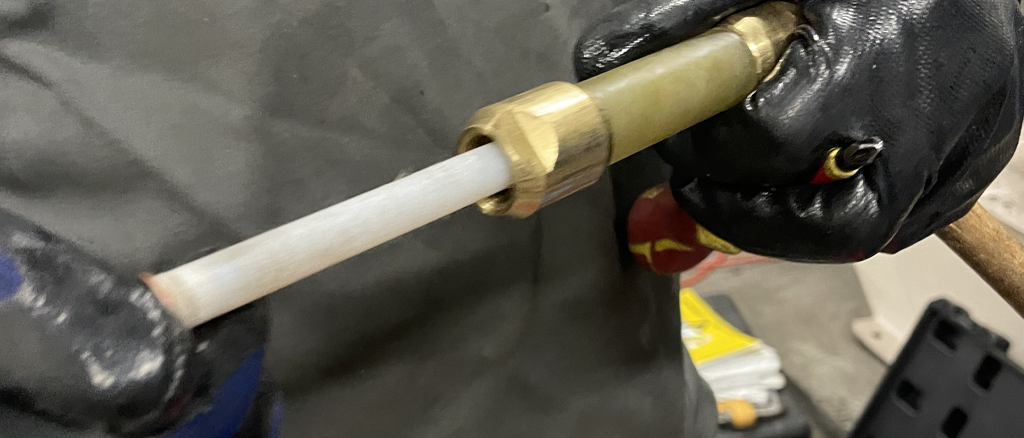 Manos enguantadas insertando una tubería blanca en un conector de latón.