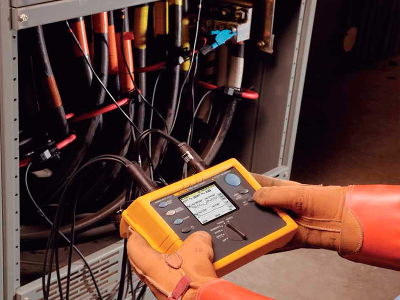 Técnico con guantes usando analizador de calidad de energía Fluke en panel eléctrico.