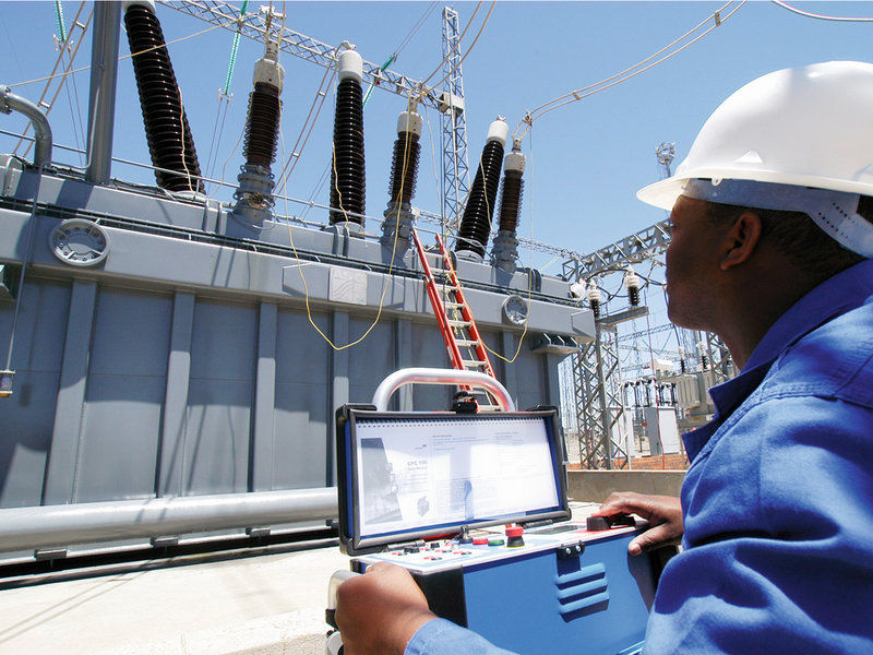 Técnico realizando mantenimiento de transformadores en una subestación eléctrica con equipo de prueba.